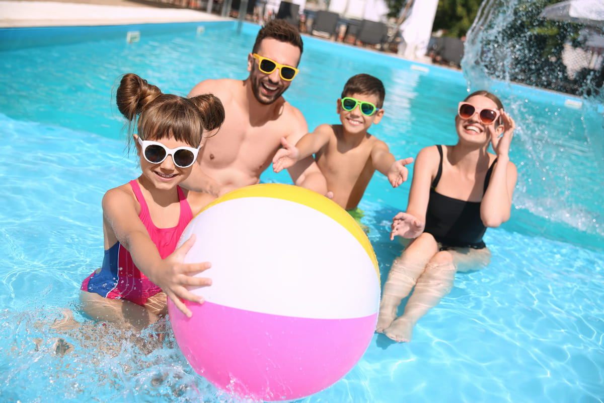 Familie cu doi copii jucandu-se cu o minge in piscina unui resort